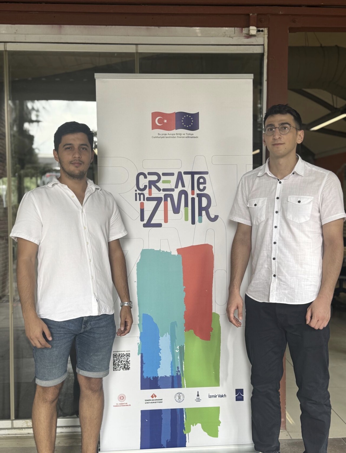 Cem Ayyıldız and Akifcan Kara standing side by side in front of the Create in İzmir banner.